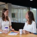 Twee pratende vrouwen met donker haar. Beide hebben ze een IZZ koffiebeker in hun handen.