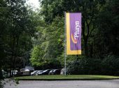 Vlag van Pluryn in geel en paars met bomen en parkeerterrein op de achtergrond