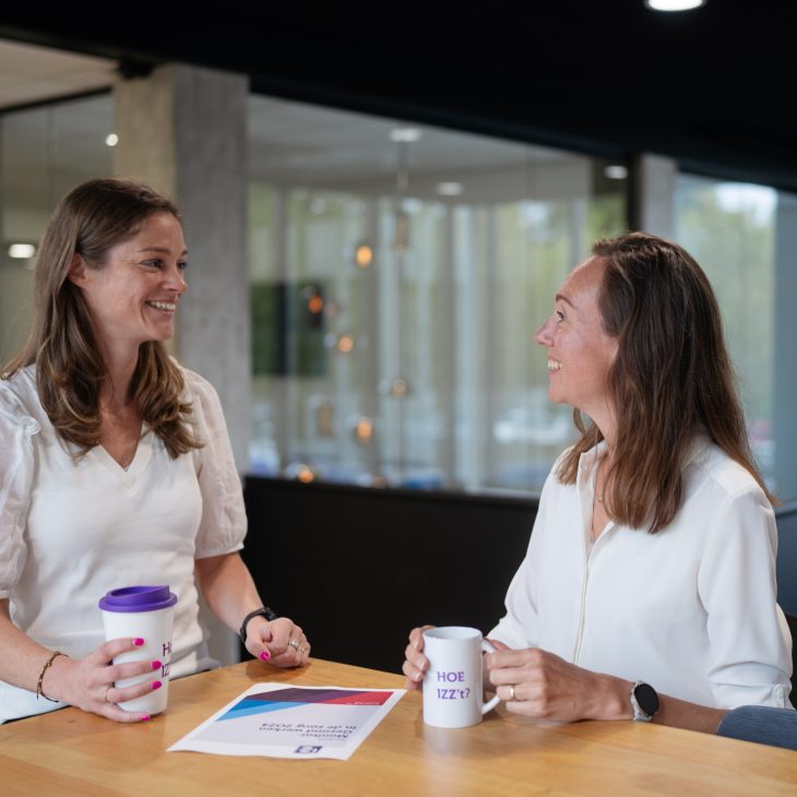 Twee pratende vrouwen met donker haar. Beide hebben ze een IZZ koffiebeker in hun handen.